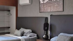 Ein Hotelzimmer mit zwei Betten, einer Wand-Klimaanlage, einem gerahmten Bild und einer Lampe auf dem Nachttisch.