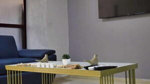 Ein modernes Wohnzimmer mit einem blauen Sofa, einem Couchtisch aus Holz mit Dekoration und einem an der Wand befestigten Flachbildfernseher.