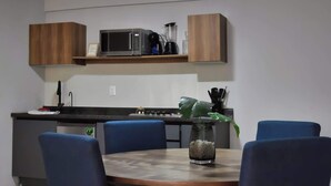 Eine moderne Küche mit Mikrowelle, Kaffeemaschine und einer Pflanze auf der Arbeitsfläche. Es steht ein runder Tisch mit blauen Stühlen und eine Vase mit Steinen darauf.