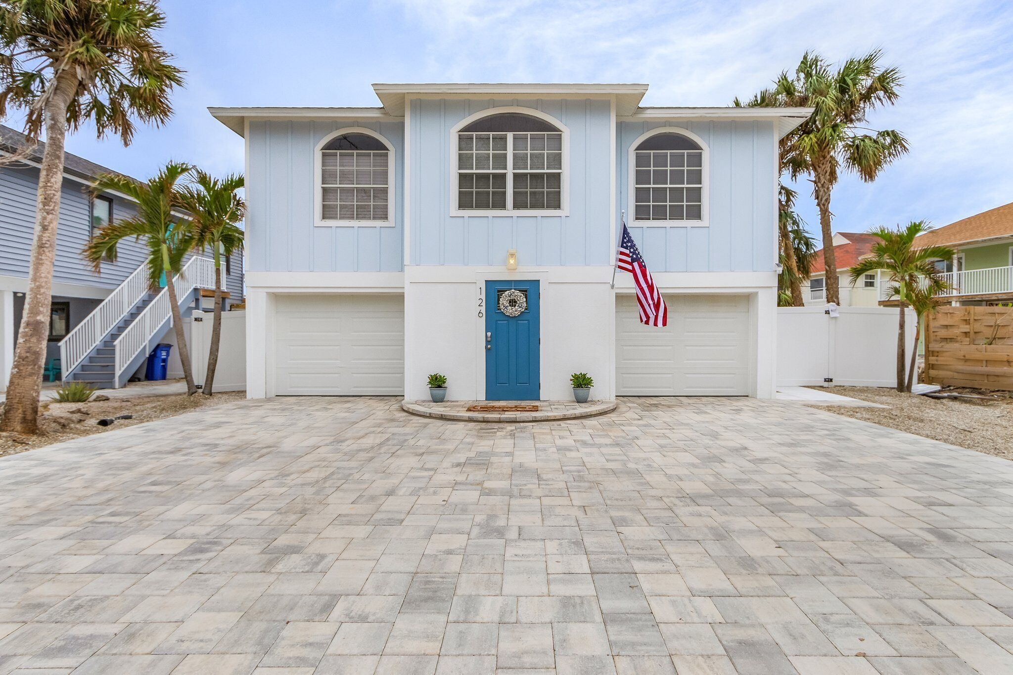 A two-story house with a blue door, an American flag, and a wreath on the front door.