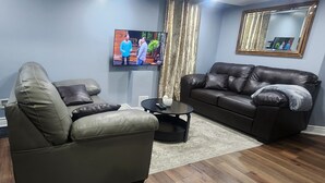 A living room with a green sofa, a black leather sofa, a coffee table, and a TV mounted on the wall.