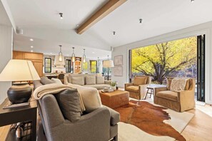 A modern living room with a sofa, chairs, a coffee table, and a large window with a view of trees.