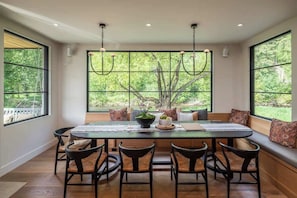 Un coin repas comprenant une grande table, six chaises et une vue sur la verdure par une fenêtre.