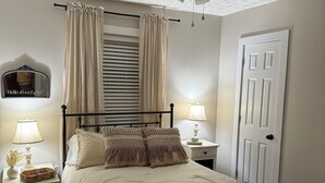 Ein Schlafzimmer mit Bett, Nachttischen, Deckenventilator, Fenster mit Vorhängen, einer Tür und einem Spiegel mit einem Schild.