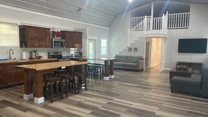 A spacious living area with a large wooden dining table, a kitchen with dark wooden cabinets, and a staircase leading to an upper level. - Charming 4-bedroom barndominum in Elberta with AC, WiFi, 5 miles from boat ramp
 (Elberta)