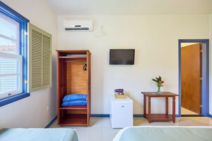 Habitación de hotel con cama, armario, una mesita con un florero, televisión y ventana con persianas.