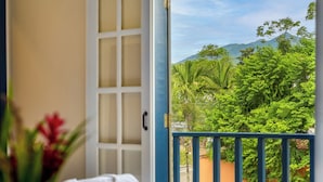 A room with a bed, a purple blanket, and a view of lush greenery and mountains through an open door. - Casa Poema Paraty (Paraty)