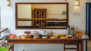 A dining area with a long wooden table set with various dishes, a chandelier, and a large mirror above the table. - Casa Poema Paraty (Paraty)