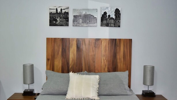 A bed with a wooden headboard, two bedside lamps, and three framed pictures on the wall.