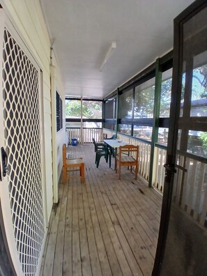 A covered porch with wooden flooring, a table, and chairs.