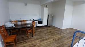 A compact kitchen with a dining area, wooden flooring, and white cabinetry. - Stay on Mer (Murray Island)