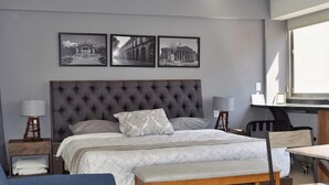 Une chambre avec un grand lit, des tables de chevet, un bureau et une chaise. Trois tableaux encadrés sont accrochés au mur au-dessus du lit.