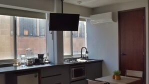 Une cuisine compacte équipée d’une cuisinière intégrée, d’un four à micro-ondes et d’un évier. On y trouve également un petit réfrigérateur, une fenêtre avec des stores et une porte dotée d’une poignée.
