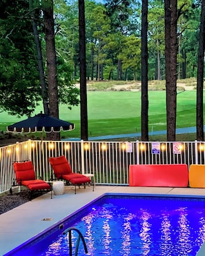 A pool area with a view of a golf course, surrounded by trees and a fence with string lights. - ThePalmerRetreat-CentralDr•SaltWaterPool•HotTub•FirePit•MinsToDT.SP/Pinehurst (Southern Pines)