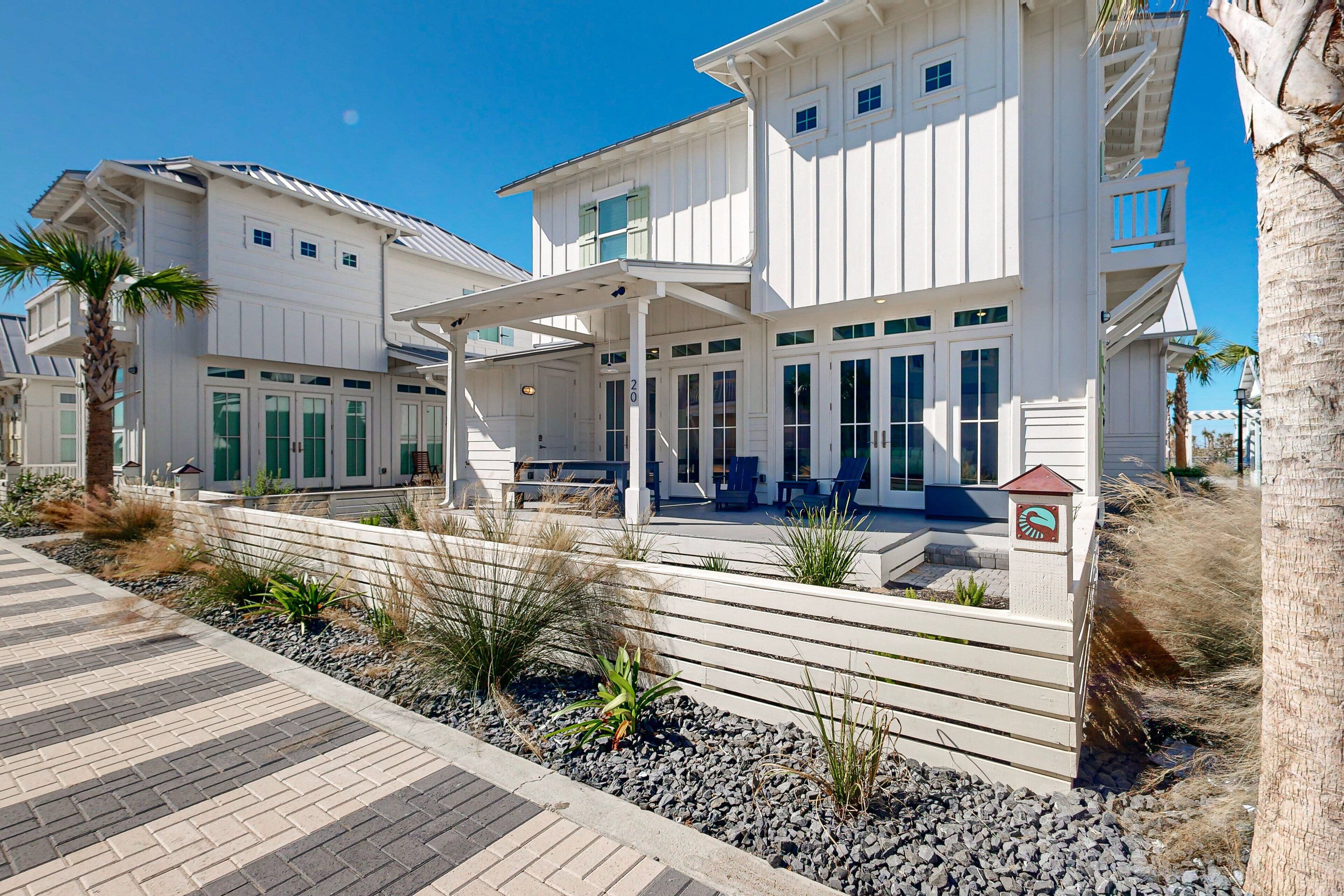 Ein großes, weißes Strandhaus mit überdachter Terrasse und Sitzbereich im Freien.