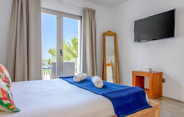 Habitación de hotel con cama, televisor, espejo y una pequeña mesita de madera.