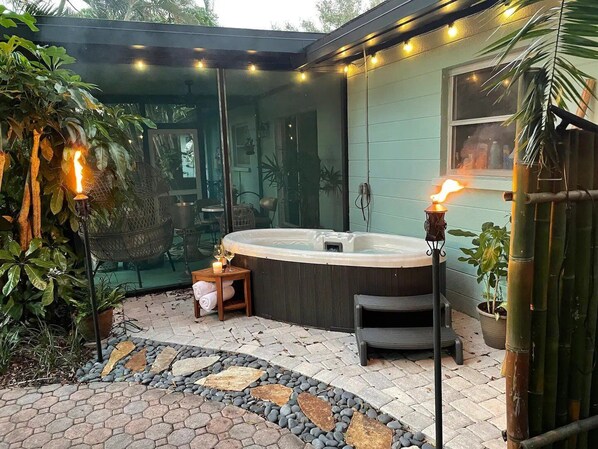 A hot tub with a stone pathway, surrounded by potted plants and outdoor furniture. - ⚓Palma Sola Oasis!  Cozy tropical home w/ Putting Green & Hot tub minutes from AMI!⚓ (Bradenton)