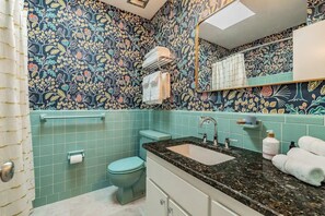 A bathroom with a floral wallpaper, a toilet, a sink with a mirror, and a towel rack. - ⚓Palma Sola Oasis!  Cozy tropical home w/ Putting Green & Hot tub minutes from AMI!⚓ (Bradenton)