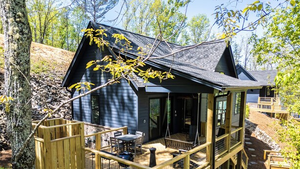 A cabin with a deck, outdoor seating, and a view of the surrounding forest. - Massive Lake Martin Estate - Sleeps 23 (Jacksons' Gap)