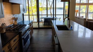 A modern kitchen with a large island, a dining area with a view of a lake, and a cozy seating area with a sofa. - Massive Lake Martin Estate - Sleeps 23 (Jacksons' Gap)