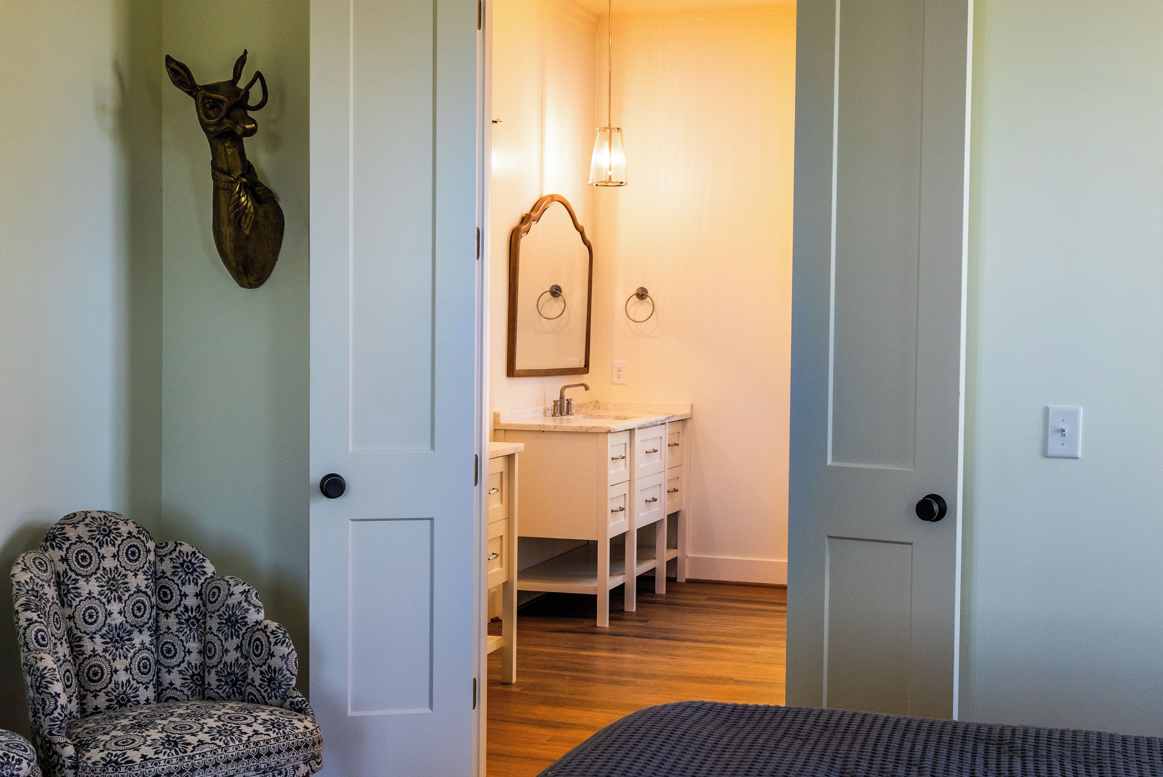 Ein Zimmer mit einem gemusterten Sessel, einer Holztür, einem Spiegel und einem Waschbecken.