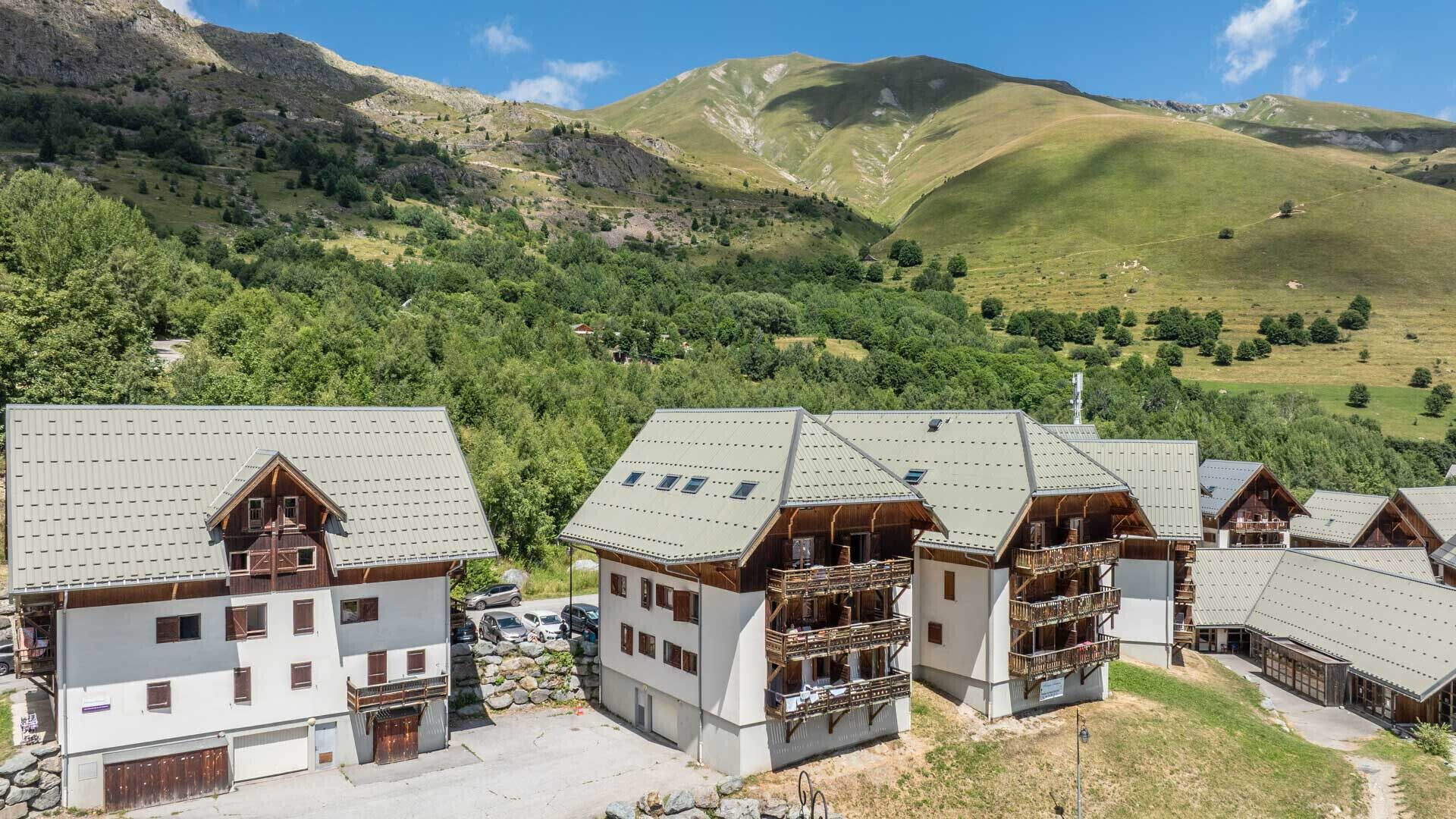 A cluster of chalet-style buildings with sloped roofs, wooden balconies, and a mountainous backdrop.