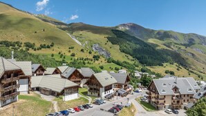 A cluster of wooden chalets with sloped roofs, set against a backdrop of green hills and a clear sky.