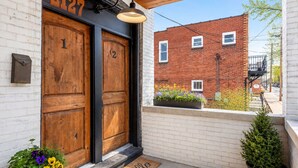 Un edificio con dos puertas de madera marcadas con los números 1 y 2, un muro de ladrillo y un pequeño jardín con flores.