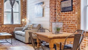 Una habitación acogedora con pared de ladrillo, una mesa de madera para comer y un sofá.