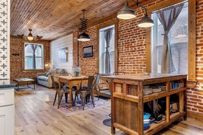 A rustic kitchen with wooden beams, a dining area with a table and chairs, and a brick wall.