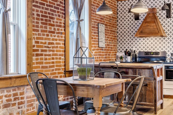 A rustic kitchen with exposed brick walls, wooden tables, and pendant lighting.