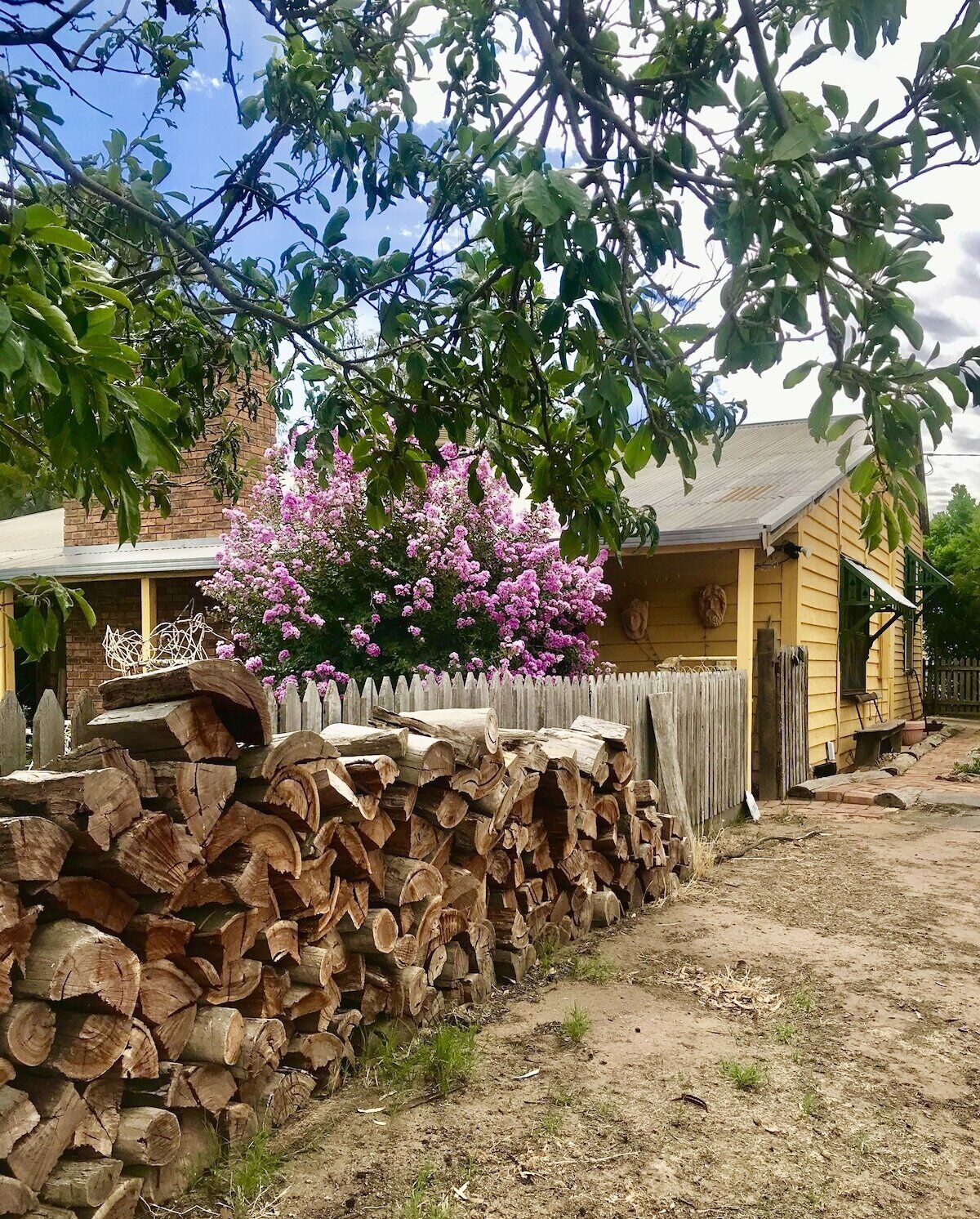 Una casa de madera rústica con un muro de piedra, un arbusto de flores rosadas y una valla de madera.