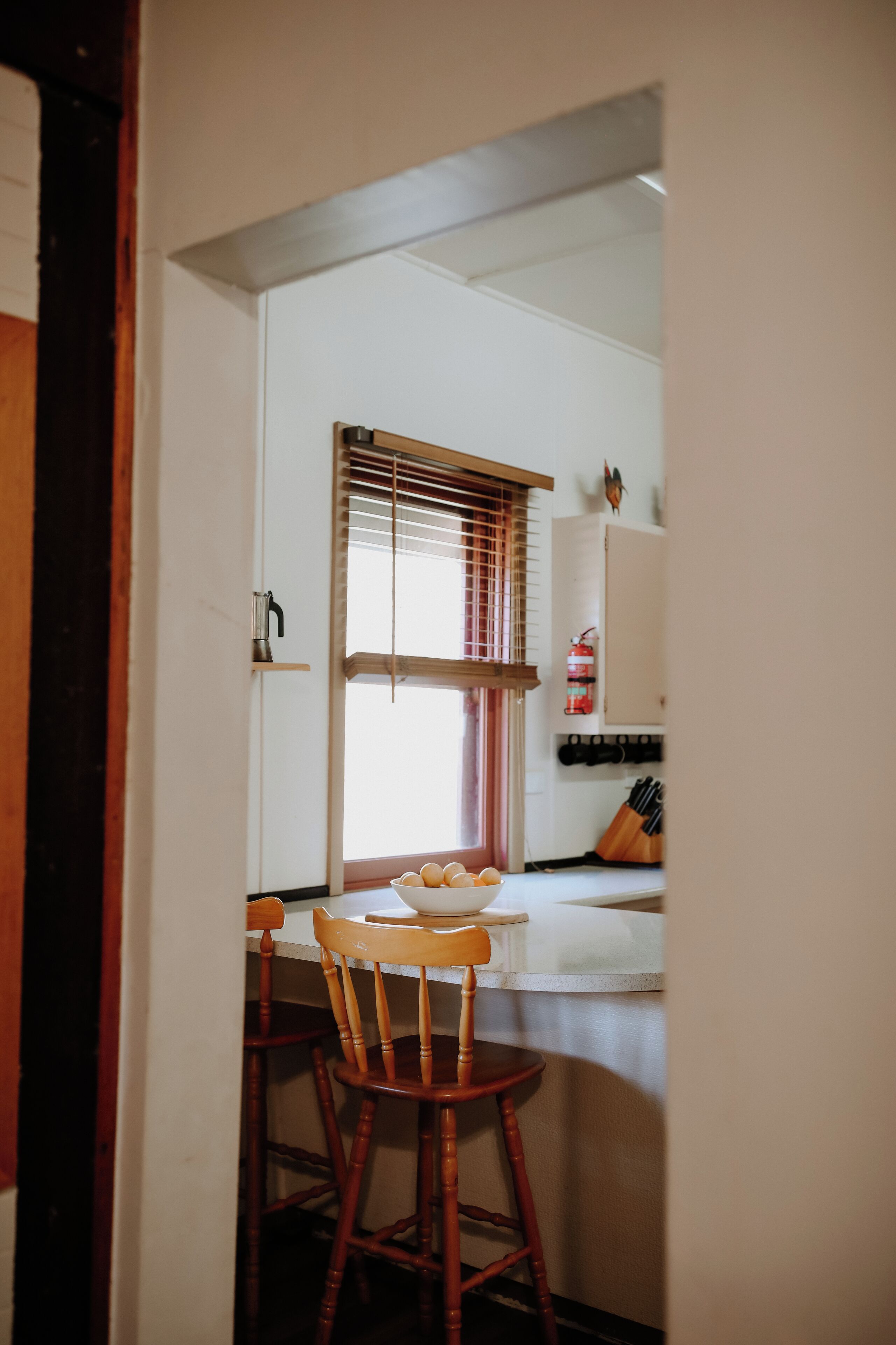 Una cocina con una silla de madera, una ventana con persianas y una encimera blanca.