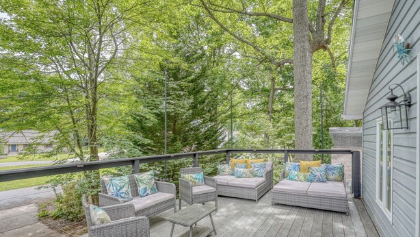 A covered outdoor deck with wicker furniture and cushions, surrounded by trees.