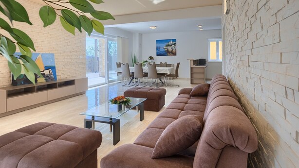 Un salon moderne avec un canapé d’angle, une table basse en verre et un coin repas comprenant une table et des chaises blanches.