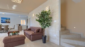 Un salon moderne avec un canapé marron, un pouf assorti, une plante en pot et un escalier menant à l’étage supérieur.