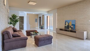 Un salon moderne avec un canapé marron, une table basse en verre et un pouf assorti. Un tableau orne le mur, et une plante en pot est posée à proximité.