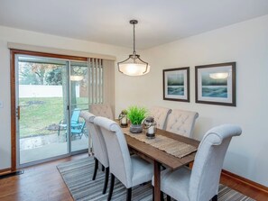 A dining area with a table, chairs, a hanging light fixture, and two framed pictures on the wall.