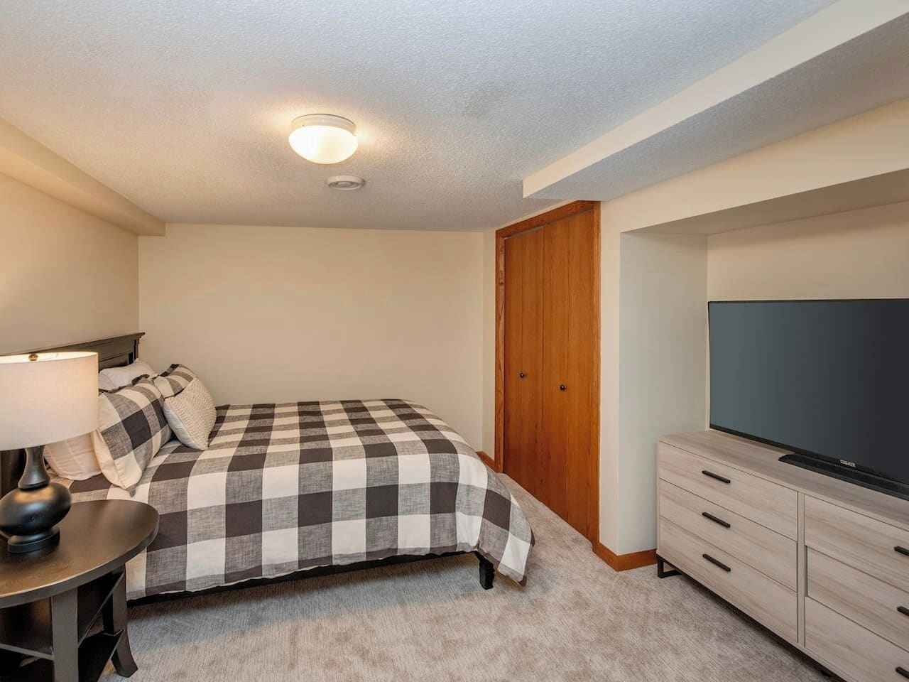 A bedroom with a bed, a TV, a desk with a lamp, and a closet.