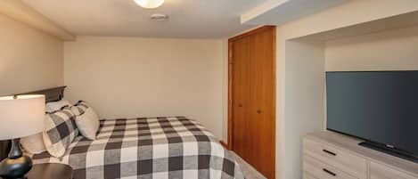 A bedroom with a bed, a TV, a desk with a lamp, and a closet.