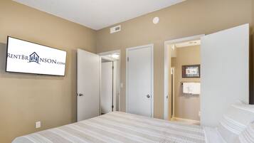 A hotel room with a bed, a television mounted on the wall, and a door leading to a bathroom.