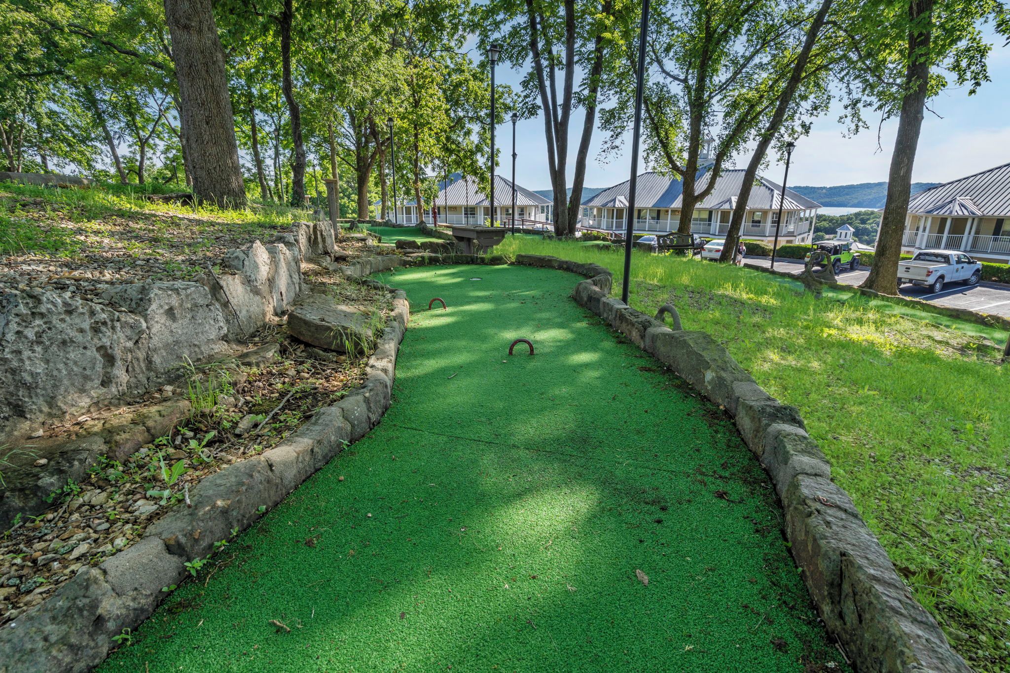 A green croquet field with stone borders, surrounded by trees and a view of buildings in the background.