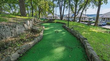 A green croquet field with stone borders, surrounded by trees and a view of buildings in the background.