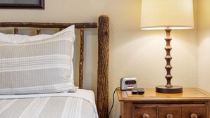 Una cama con ropa de cama blanca y a rayas, una mesita de noche de madera con una lámpara y un reloj digital que marca las 23:33.