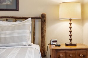 A bed with white and striped bedding, a wooden nightstand with a lamp, and a digital clock displaying 23:33. - Charming Escape with Scenic Wood Views, Walk-to-Lake Access, Outdoor Pool & Free Attraction Tickets (Kimberling City)