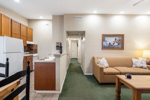 A compact living space with a kitchenette, a sofa, a coffee table, and a hallway leading to another room.