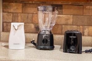 A Proctor Silex blender, a white charging cable, and a black toaster on a countertop. - Charming Escape with Scenic Wood Views, Walk-to-Lake Access, Outdoor Pool & Free Attraction Tickets (Kimberling City)