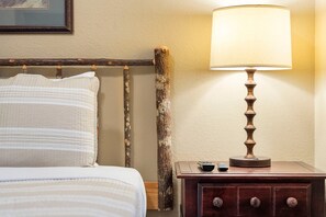 A bed with a striped pillow, a wooden nightstand with a lamp, and a remote control.
