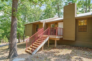 Une maison à deux étages avec un escalier en bois et une rampe rouge, entourée d’arbres.