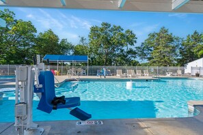 A swimming pool with a lifeguard stand, lounge chairs, and a fenced area with trees in the background.